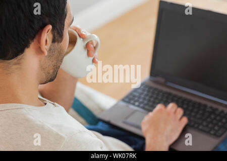 Handsome brown haired man drinking coffee while using his laptop Stock Photo