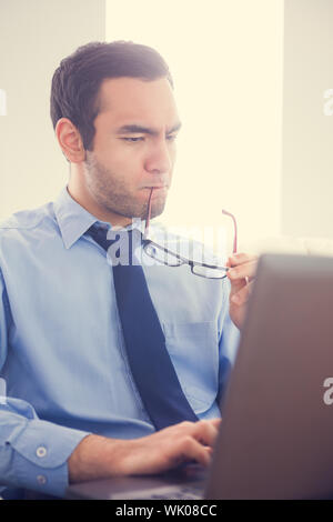 Focused man biting his eyeglasses and using a laptop Stock Photo