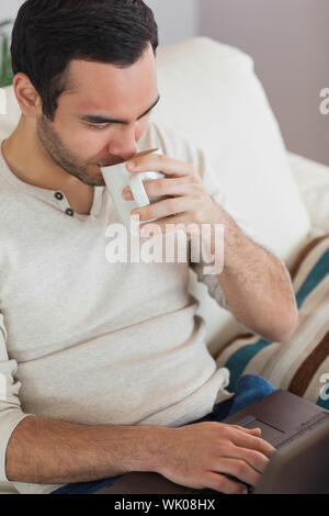 Peaceful attractive man drinking coffee while using his laptop Stock Photo