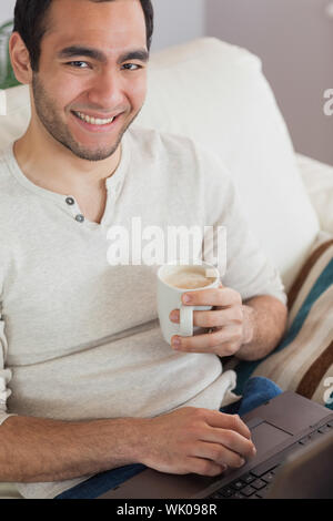 Smiling attractive man drinking coffee while using his laptop Stock Photo