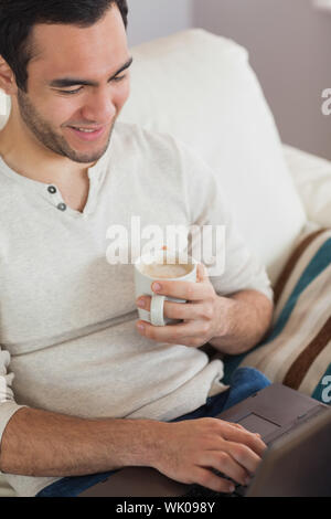 Calm attractive man drinking coffee while using his laptop Stock Photo