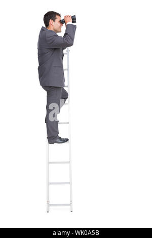 Businessman standing on ladder using binoculars Stock Photo