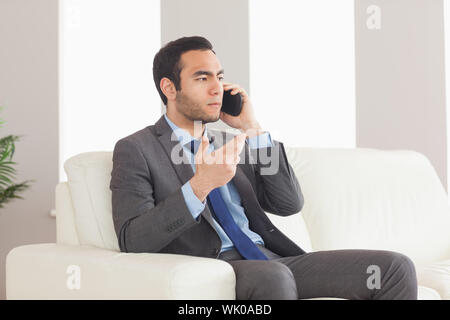 Serious businessman on the phone sitting on cosy sofa Stock Photo