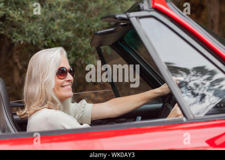 Happy mature woman with sunglasses driving red convertible Stock Photo
