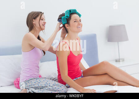 Girls sitting in bed one wearing hair rollers Stock Photo