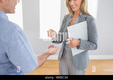 Close up of a smiling realtor delivering a key to a laughing buyer Stock Photo