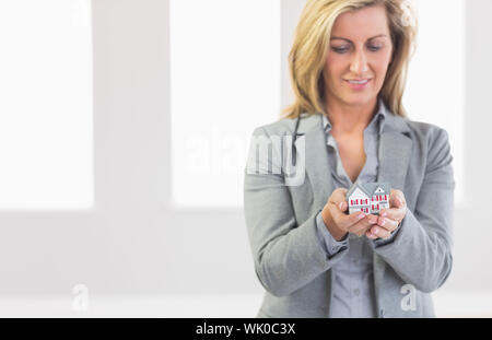 Thoughtful realtor standing looking and presenting a mini model house Stock Photo