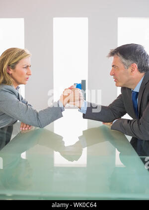 Two annoyed businesspeople having an arm wrestling sitting around a table Stock Photo