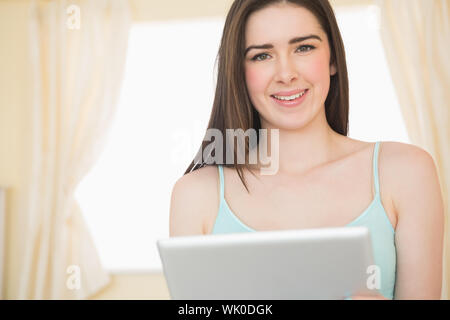 Smiling young woman looking and using a tablet pc sitting on her bed Stock Photo