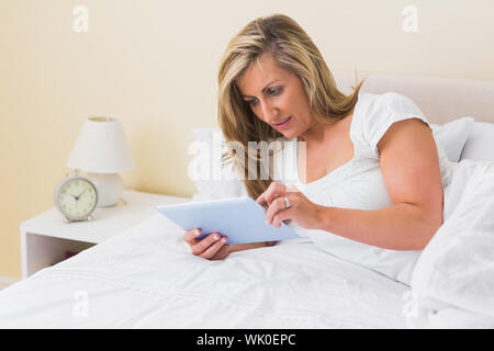 Thoughtful woman using a tablet pc lying on her bed Stock Photo