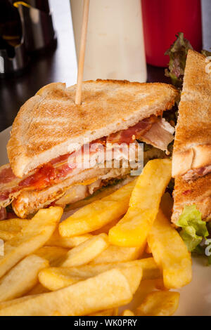 Club sandwich on toasted white bread with a meat filling served with crispy golden potato French fries, closeup partial view isolated on white Stock Photo