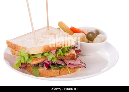 Delicious thinly sliced beef pastrami club sandwich with fresh curly lettuce served with a small dish of pickled vegetables on a white plate, isolated Stock Photo