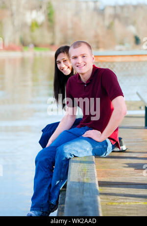 Beautiful young interracial couple sitting on wooden dock over lake, dangling feet over sides Stock Photo