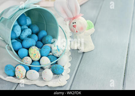 A blue tin bucket tipped over, spilling Easter candy eggs onto a table. Shallow depth of field. Stock Photo