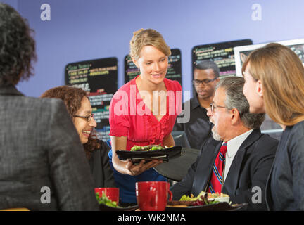 Young barista serving smiling executives food in cafe Stock Photo