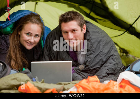 A happy couple in a tent using a computer looking at the camera Stock Photo