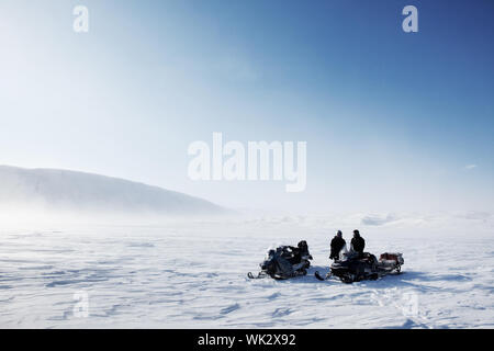 Three snowmobiles on a winter landscape with blowing snow Stock Photo