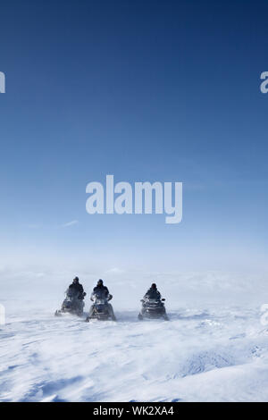 Three snowmobiles on a winter landscape with blowing snow Stock Photo