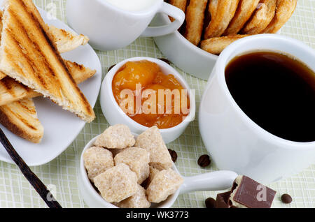 Breakfast with Cup of Coffee, Chocolate, Sugar Cubes, Toasts, Apricot Jam, Milk and Puff Pastry on Checkered background Stock Photo