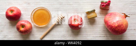 Rosh Hashanah (Jewish New Year holiday) concept. Traditional symbols - apples, honey, pomegranate on white linen background, top view, banner. Stock Photo