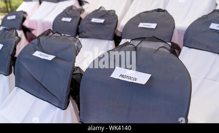 Reserved chairs in a row for protocol. Reserved chairs in a row for VIP. Chairs covered by white and grey cloth. Stock Photo