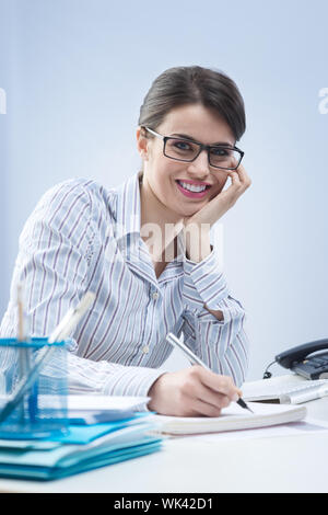 Young attractive businesswoman writing down notes and smiling. Stock Photo