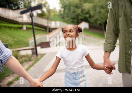 Daughter making funny face while walking with parents Stock Photo