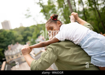 Strong father lifting his cute lovely dark-skinned girl Stock Photo