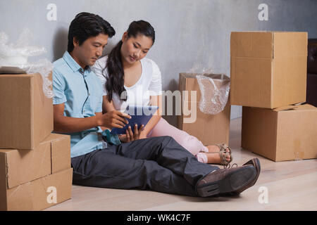 Happy couple sitting on floor using tablet in their new home Stock Photo