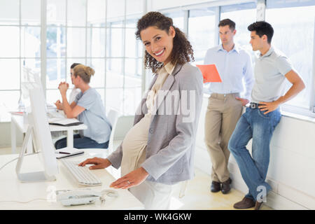 Pregnant businesswoman smiling at camera with team behind her in the office Stock Photo