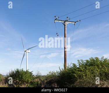 Crick, Northamptonshire, UK: A wooden electricity power pole stands in front of a wind turbine under a blue sky and whispy clouds. Stock Photo