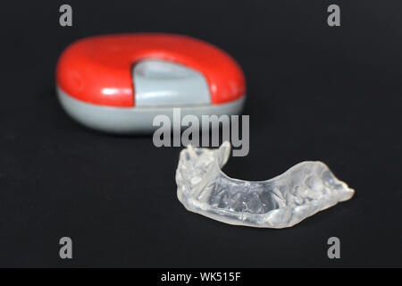 Customized transparent dental teeth bite guard clear aligners for lower jaw in front of blurry case on dark black Stock Photo