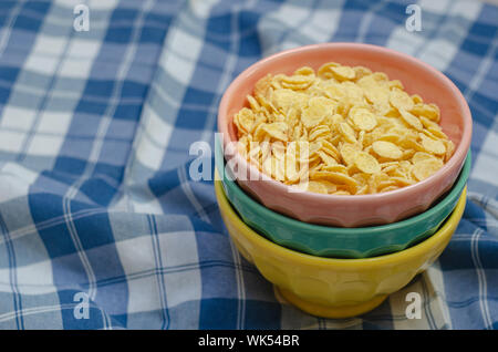 Cornflakes and three bowls of different colors, on a plaid napkin in blue and white. copy space. Stock Photo
