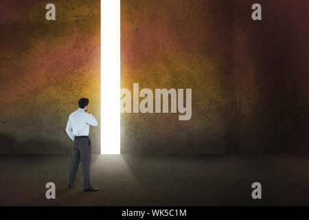 Thoughtful businessman with hand on chin against door revealing bright light Stock Photo