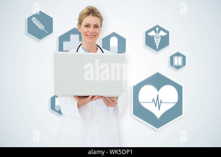 Blonde doctor using laptop against blue medical interface with icons Stock Photo