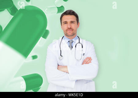Handsome young doctor with arms crossed against green medical background with pills Stock Photo
