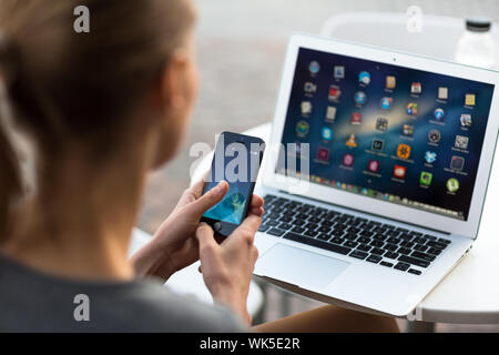 Portrait of a sleek young woman using her smartphone and her laptop in a an urban/city context (shallow DOF; color toned image) Stock Photo
