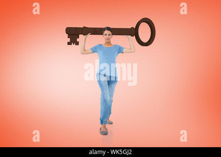 Composite image of annoyed brunette carrying large key against orange Stock Photo