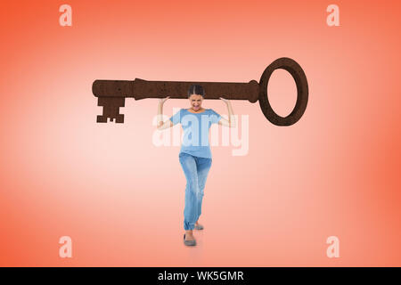 Composite image of annoyed brunette carrying large key on orange background Stock Photo