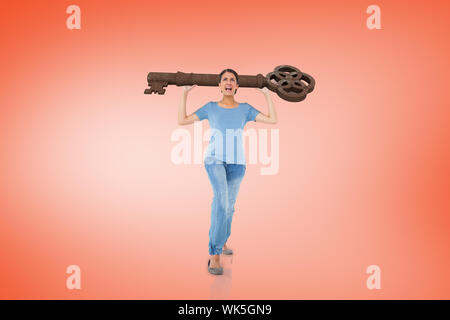 Composite image of annoyed brunette carrying large key on orange background Stock Photo
