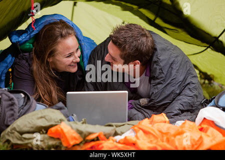 A happy couple in a tent using a computer looking at each other Stock Photo
