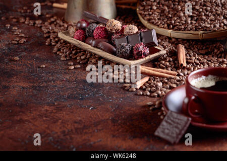 Chocolates  and cup of black coffee. Sweets with cinnamon sticks and coffee beans on a brown table. Selective focus. Stock Photo