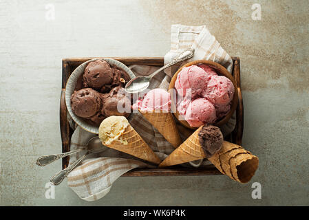 Ice cream scoops with chocolate, strawberry and vanilla flavors, scooped in to waffle cones and bowls Stock Photo