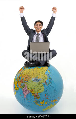 Businessman sitting on a globe and using a laptop with celebrating success Stock Photo