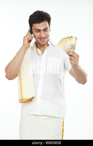 South Indian man talking on a mobile phone and holding Indian banknotes Stock Photo