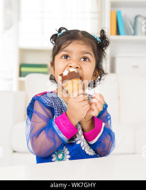 Eating ice cream. Indian Asian girl enjoying an ice cream. Beautiful child model at home. Stock Photo