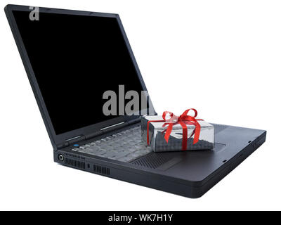 Small gift wrapped with a red ribbon over a black laptop isolated on white. Black copy space on screen. Stock Photo