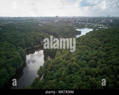 The river flows in the forest against city landscape at the background. Aerial view. Stock Photo