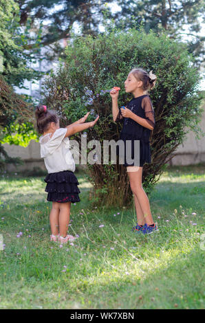 Two cute sisters are playing with soap bubbles in the garden Stock Photo