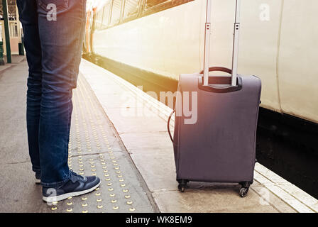 Man traveller with suitcase near him standing on the train platform Stock Photo